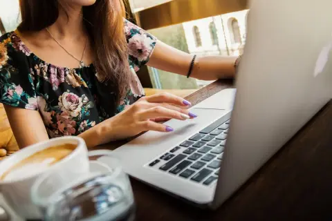 Ragazza con laptop e caffè, mentre cerca la differenza ferie e permessi.