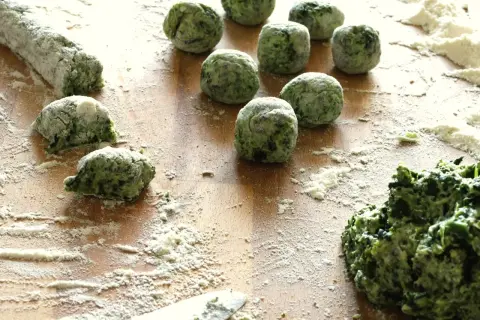 Zielone, domowe gnocchi ze szpinakiem, obtoczone mąką, czekają na ugotowanie.