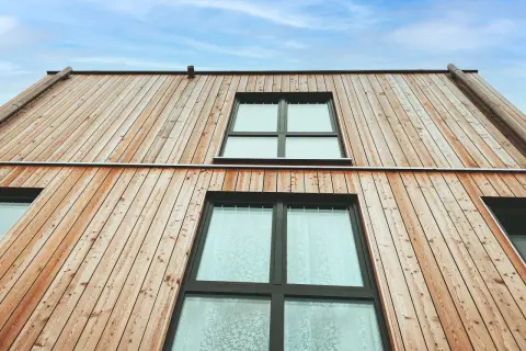 Moderne Holzfassaden Beispiele: Natürliche Holzverkleidung mit großen Fenstern unter blauem Himmel.