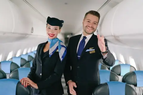 Uśmiechnięci steward i stewardessa w uniformach LOT. Spełniają wymagania, by zapewnić komfort podróży.