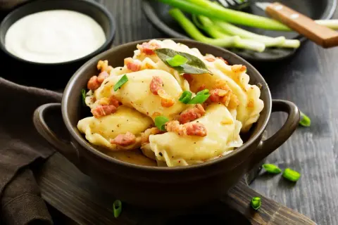 Pyszne pierogi z boczkiem i szczypiorkiem. Wiesz, ile gotować pierogi, by były idealne? Podane z kwaśną śmietaną.