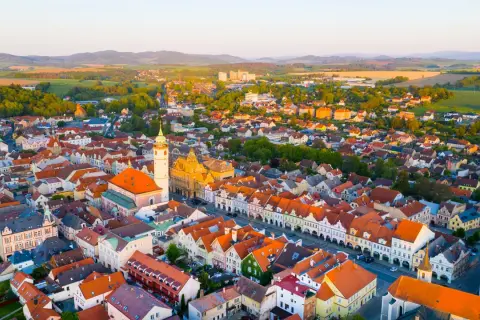 Luftaufnahme eines malerischen **Taus Tschechien** mit roten Dächern, einer Kirche und grünen Hügeln im Hintergrund.