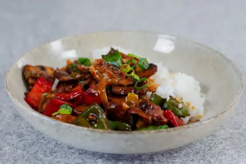 En skål med ris och en smakrik kyckling cashew-rätt med paprika och svamp, toppad med salladslök.