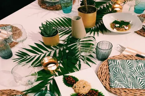Une table dressée dans une ambiance jungle, avec des feuilles de palmier, des plantes en boîtes et des bougies.