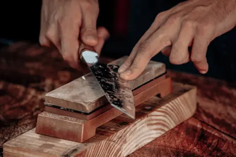 Manos afilando un cuchillo con una piedra de afilar. Aprende como afilar cuchillos con afilador para un corte perfecto.