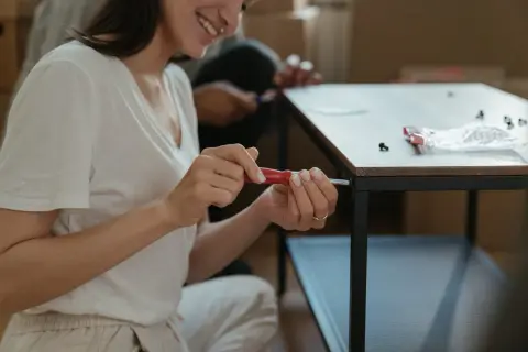 Kobieta z uśmiechem próbuje odkręcić wyrobioną śrubę krzyżakową, składając meble.