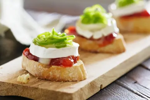 Deliciosos pinchos y tapas originales: rebanadas de pan con queso de cabra, mermelada de pimientos y cebolla morada.