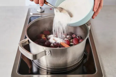 Zucker wird zu Trauben und Zimt in einem Topf gegeben, um köstliche Weintrauben Marmelade herzustellen.