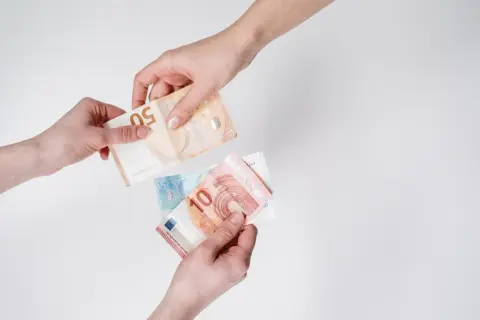 Dwie ręce przekazują sobie banknoty euro. To popularna waluta we Włoszech, używana do codziennych transakcji.