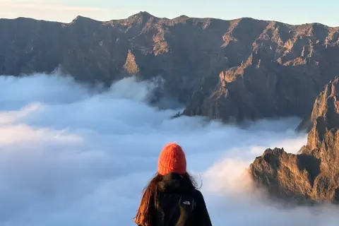 Widok na góry i morze chmur, jak na La Isla Bonita po polsku. Słońce oświetla skaliste szczyty.