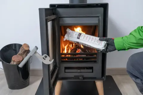 Persona con guantes verdes y grises introduce un producto envasado en una chimenea encendida. Es parte de la limpieza de chimeneas.
