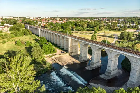 Kamienny wiadukt kolejowy nad rzeką, z miastem w tle. Bolesławiec atrakcje, które zachwycają.