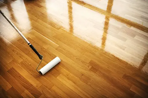 Rodillo aplicando barniz a un suelo de parquet de madera, restaurando su brillo. Mantenimiento parquet.