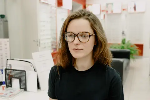 Młoda kobieta w okularach w panterkę, z lekko przekrzywionym wzrokiem, jakby szukała czegoś ukrytego.