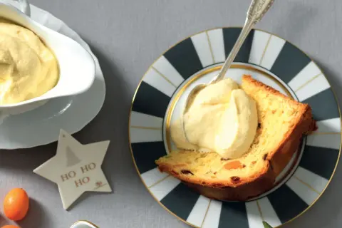 Una fetta di panettone con abbondante crema al mascarpone, servita su un piatto decorato. Un'idea golosa per le feste.
