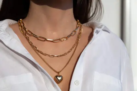 Tres collares dorados en capas, uno con un corazón, lucen perfectos con el escote de una camisa blanca.
