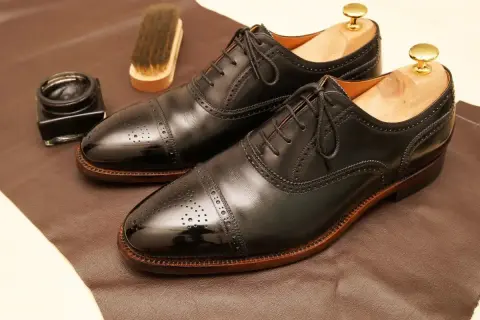 Paire de richelieus noirs brillants, prêts pour un glacage chaussure parfait. Pot de cirage et brosse à proximité.