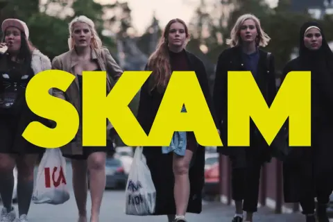 Fem tjejer går på gatan, med stora gula bokstäver som bildar ordet SKAM. En av dem dricker ur en flaska.