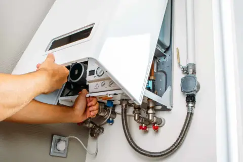 Tecnico che regola la pressione del gas dello scaldabagno, mostrando i collegamenti idraulici e il pannello di controllo.