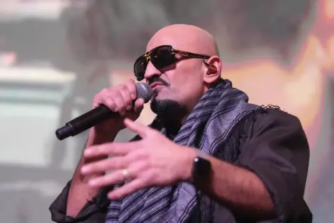 Ein bekannter Rapper mit Sonnenbrille und Schal spricht ins Mikrofon, während er gestikuliert.