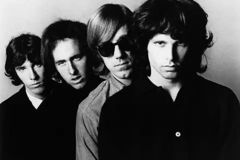 Członkowie The Doors, czwórka młodych mężczyzn z burzą włosów, patrzą w obiektyw. Jeden z nich ma okulary przeciwsłoneczne.