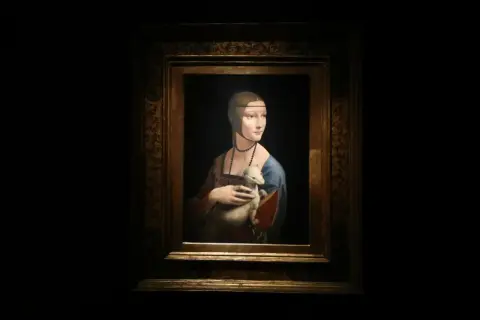 Obraz Dama z łasiczką, Leonarda da Vinci. Młoda kobieta w niebieskiej sukni trzyma w ramionach białego zwierzątko.