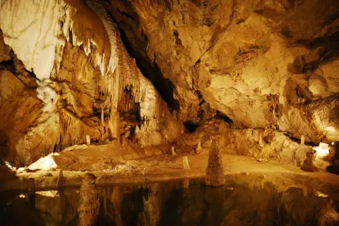 Wnętrze jaskini z naciekami i stalagmitami, odbijającymi się w wodzie. Tajemnicze piękno Tatr Bielskich.