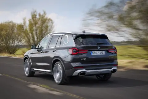 Ciemnoszary BMW X3 xDrive pędzi po drodze, otoczony zielenią i rozmazanymi drzewami.
