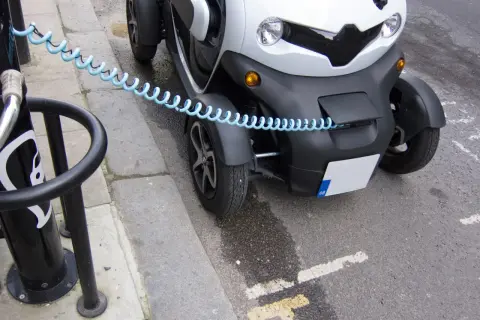 Biały, trójkołowy pojazd elektryczny podłączony do ładowarki. To pokazuje, jak zbudować samochód elektryczny, zaczynając od ładowania.