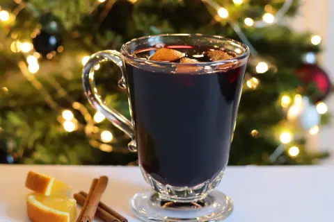 Verre de vin chaud sans alcool, garni d'orange et de cannelle, devant un sapin de Noël illuminé. Parfait pour une recette festive et réconfortante.