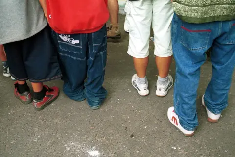 Luźne spodnie, szerokie nogawki i sportowe buty – to wszystko w stylu hip hop. Grupa młodych ludzi w luźnych ubraniach.