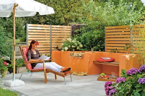 Entspannter Garten mit selbst gebautem Wasserfall. Eine Frau liest unter einem Sonnenschirm.