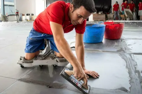 Un trabajador con rodilleras aplica cemento para saber como poner baldosas en el suelo.