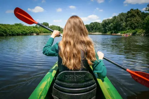 Dziewczyna wiosłuje kajakiem po spokojnej rzece, ciesząc się piękną pogodą. Idealne miejsce na spływy kajakowe Śląsk.