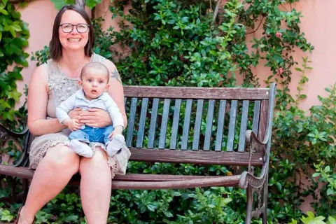 Madre sonriente abraza a su bebé en un banco. Un ejemplo de los hermosos testimonios de hijos nacidos por ovodonación.