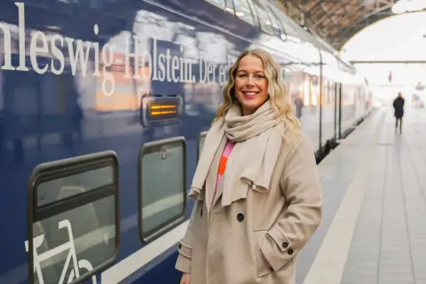 Frau am Bahnsteig in Schleswig-Holstein, bereit für neue Abenteuer. Hier sind einige Flensburg Tipps für deine Reise!