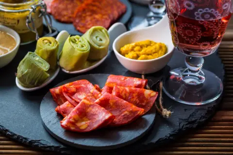 Leckere Tapas Ideen: Chorizo, eingelegte Artischocken und Senf mit einem Glas Rotwein.