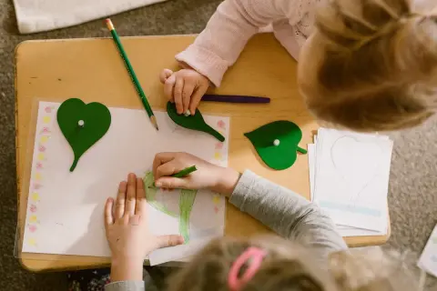 Children engage in Montessori fine motor activities, drawing and manipulating leaf shapes on a wooden table.