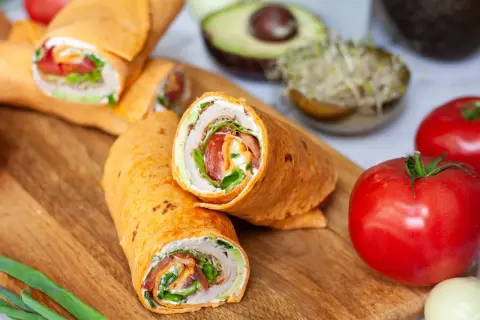 Pyszna tortilla z szynką, świeżymi warzywami i kremowym serkiem, ułożona na desce z dodatkami.