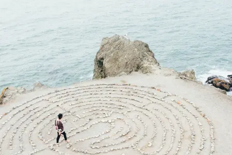 Person geht durch einen Steinlabyrinth am Meer. Ein Symbol für die Ausbildung zum spirituellen Coach, die Suche nach innerer Klarheit.