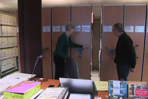 Deux personnes devant des rayonnages d'archives mobiles.