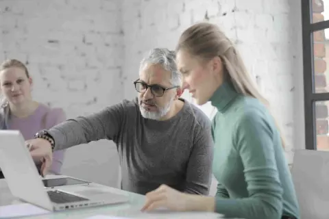 Uomo della generazione boomer spiega qualcosa su un laptop a una collega.