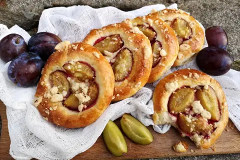 Pyszne drożdżówki ze śliwką, posypane kruszonką, prezentują się apetycznie obok świeżych śliwek.
