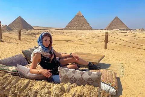 Mujer con velo descansa ante las pirámides de Giza. El sol brilla, un día perfecto, la mejor época para ir a Egipto.