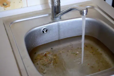 Verstopfter Abfluss im Haus? Salz als Hausmittel könnte helfen. Das Spülbecken ist voller Essensreste und steht unter Wasser.