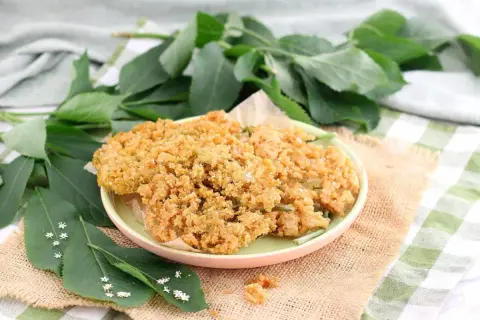 Fiori di sambuco fritti dorati e croccanti su un piatto, con foglie verdi e piccoli fiori di sambuco tutt'intorno.