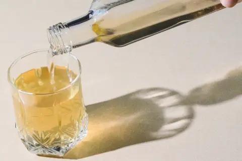 Klarer Flüssigkeit wird aus einer Glasflasche in ein Glas gegossen. Ein gesunder Schluck Essigwasser für den Tag.