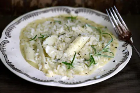 Krämig risotto med sparris och rosmarin, perfekt för ett svamprisotto recept. Serveras på en vacker tallrik med en gaffel.