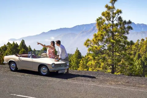 Pareja planeando sus rutas en coche por La Palma, con un descapotable y un paisaje montañoso de pinos.