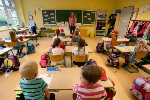 Ein helles Klassenzimmer, bereit für den Unterricht. Kinder sitzen an ihren Tischen, Rucksäcke und Lernmaterialien sind schon da. Das Klassenzimmer einrichten ist abgeschlossen.